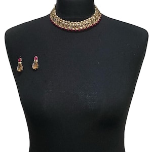 Puede incluir: Un collar choker dorado con piedras en forma de lágrima y detalles rosas. Pendientes a juego con piedras en forma de lágrima y detalles rosas.
