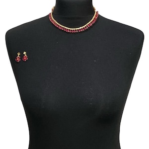 May include: A gold necklace with a row of dangling red teardrop-shaped stones. Matching red stone earrings are included.