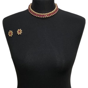 Könnte beinhalten: Eine goldene Halskette mit rosafarbenen ovalen Steinen und weißen Perlen sowie passende Ohrringe mit rosafarbenen Steinen. Die Halskette befindet sich auf einer schwarzen Schaufensterpuppe.