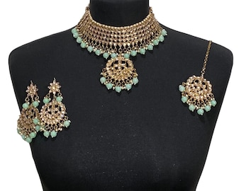 May include: A gold and mint green Indian bridal jewelry set with a choker necklace, earrings, and a maang tikka.