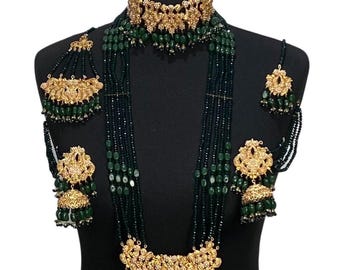 Puede incluir: Un conjunto de collar de novia tradicional indio en color dorado y verde. El conjunto incluye un collar largo con múltiples hileras de cuentas verdes, un collar gargantilla, pendientes y un maang tikka.