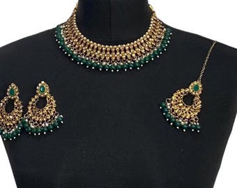以下が含まれることがあります： ネックレス、イヤリング、ヘアアクセサリーを含むゴールドトーンのジュエリーセット。セットは緑色のビーズと宝石で飾られています。ネックレスとイヤリングは詳細で装飾的なデザインで、ヘアアクセサリーは繊細なチェーンで接続されています。