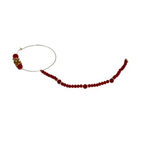 May include: A red beaded nose ring with a gold charm. The nose ring is made of a thin wire and has a chain that hangs down from the ring.