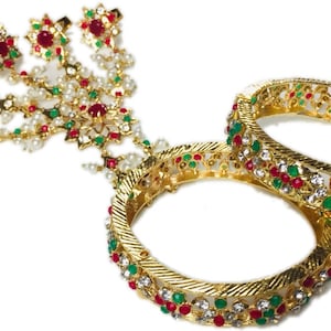 May include: A set of gold bangles featuring red and green stones, and white pearls. The bangles are adorned with intricate designs and are ideal for adding a touch of sparkle to any outfit.