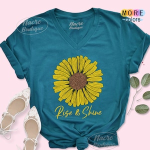 May include: Teal blue v-neck t-shirt with a yellow sunflower graphic and the text "Rise & Shine".