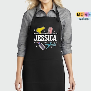 Puede incluir: Delantal negro con un bolsillo blanco y un dise&ntilde;o con un secador de pelo, un peine, unas tijeras y el nombre "JESSICA".