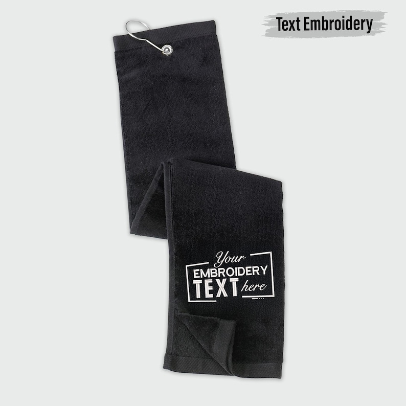 A black towel with white text embroidered on it, along with a metal hook attached to the top of the towel.
