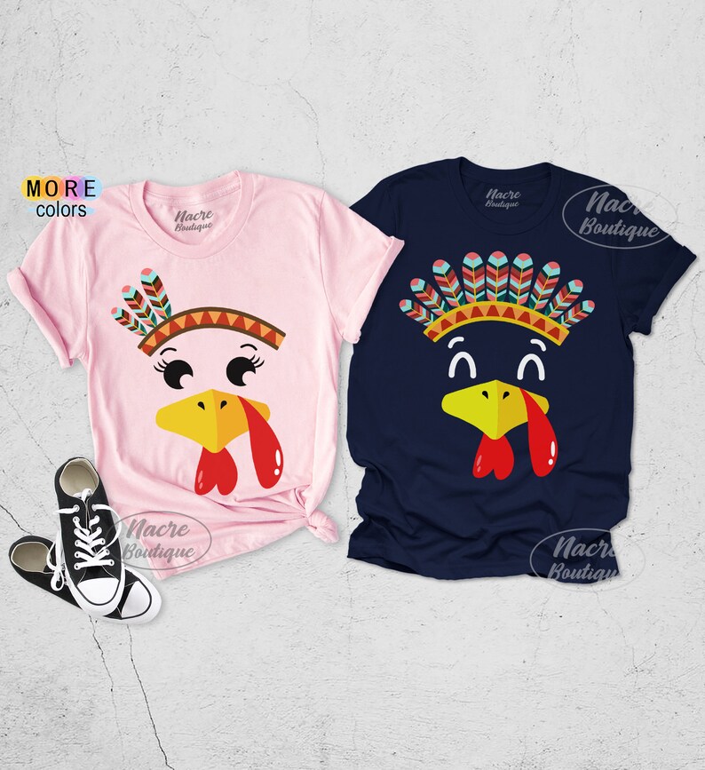 May include: Two short-sleeved t-shirts with turkey face designs. One is light pink, the other is navy blue. Each shirt features a turkey face with a yellow beak, red wattle, and a Native American headdress. The brand name "Nacre Boutique" is printed on the shirts.