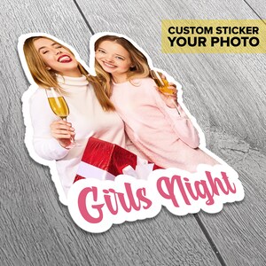 Puede incluir: Dos amigas sonrientes sosteniendo copas de champ&aacute;n. Est&aacute;n sosteniendo una caja de regalo roja con una cinta blanca. El texto "Girls Night" est&aacute; escrito en rosa sobre un fondo blanco.