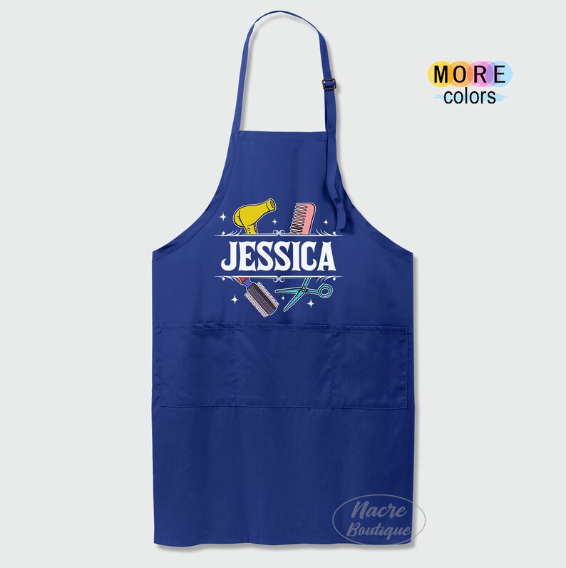 Puede incluir: Delantal azul con un bolsillo, que presenta un secador de pelo, tijeras y un peine con el nombre "JESSICA" impreso en blanco.