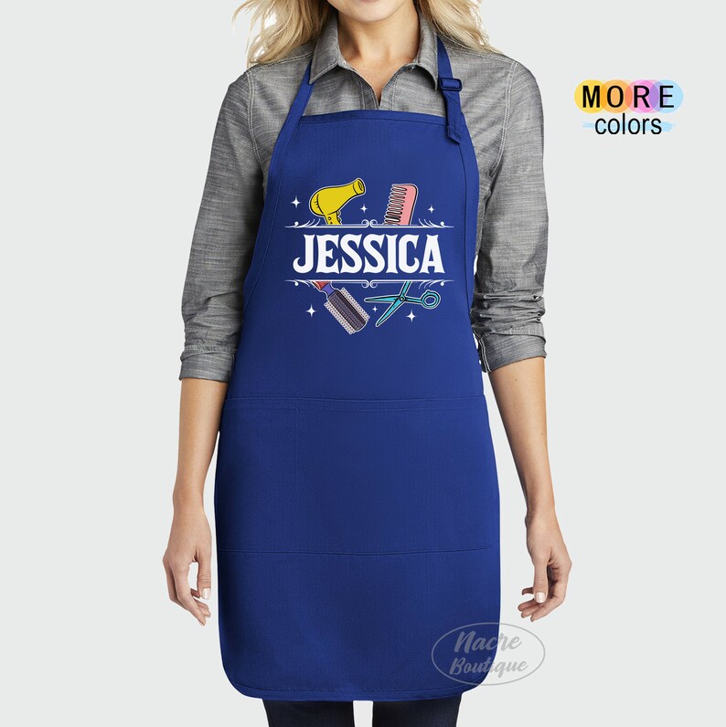 Puede incluir: Delantal azul con un dise&ntilde;o blanco que incluye un secador de pelo, un peine, unas tijeras y el nombre "JESSICA".
