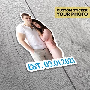 Puede incluir: Una pegatina personalizada con una foto de una pareja, el hombre lleva una camiseta blanca y pantalones caqui, la mujer lleva una camisa rosa y una falda. La pegatina tiene el texto "EST. 09.01.2021" y las palabras "CUSTOM STICKER YOUR PHOTO" en un recuadro amarillo.