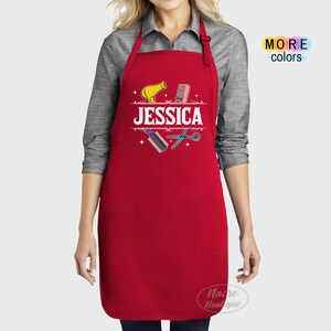 Puede incluir: Delantal rojo con un bolsillo blanco y un dise&ntilde;o con un secador de pelo, un peine, unas tijeras y el nombre "JESSICA".