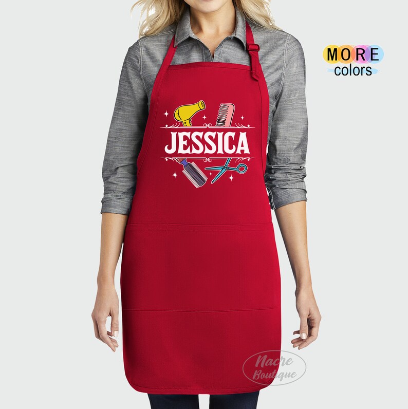Puede incluir: Delantal rojo con un bolsillo blanco y un dise&ntilde;o con un secador de pelo, un peine, unas tijeras y el nombre "JESSICA".