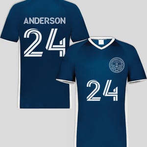 May include: Navy blue soccer jersey with white trim and the number 24 in white. The back of the jersey displays the name "ANDERSON" above the number 24. A football club logo is on the front.