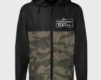 May include: A black and camouflage print hooded windbreaker jacket with a full-length front zipper and long sleeves. The upper chest area features a white rectangular graphic with the text Your EMBROIDERY TEXT here in a stylized font.