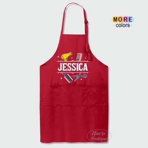 Puede incluir: Delantal rojo con un dise&ntilde;o blanco de herramientas de peluquer&iacute;a y el nombre "JESSICA".