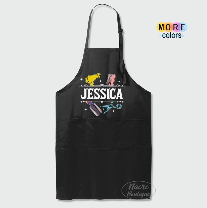 Puede incluir: Delantal negro con un bolsillo y un dise&ntilde;o de herramientas de peluquer&iacute;a, incluyendo un secador de pelo, tijeras y un peine. El texto "JESSICA" est&aacute; impreso en el delantal.