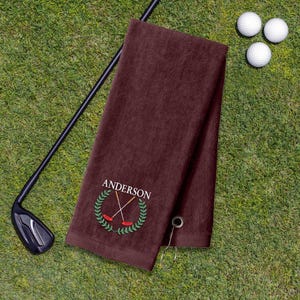 A dark brown towel with a golf club and three golf balls on a grassy surface.