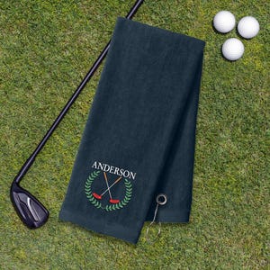 A dark green towel with a golf club and three golf balls on a grassy surface.