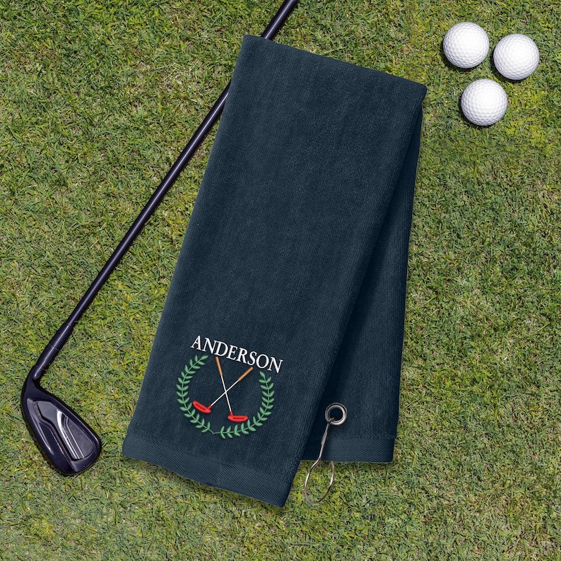 A dark green towel with a golf club and three golf balls on a grassy surface.