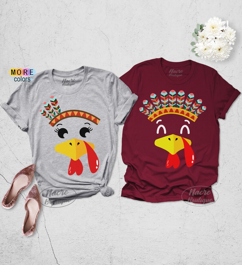 May include: Two short-sleeved t-shirts, one gray and one burgundy, feature a cartoon turkey face design. The turkey has a yellow beak, red wattle, and a colorful headdress. The text "MORE colors" is visible on the left.