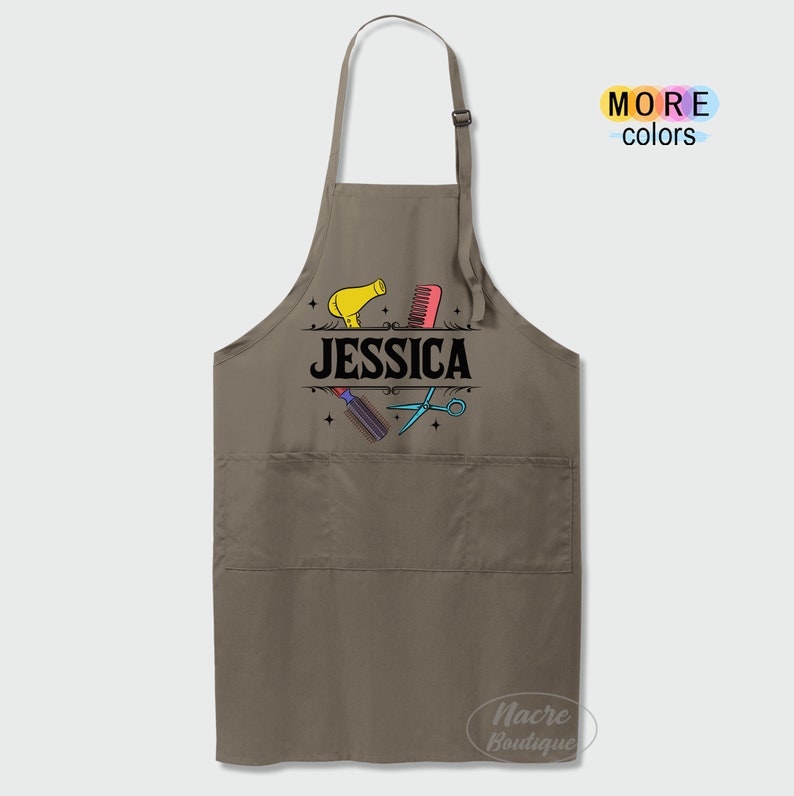 Puede incluir: Un delantal marr&oacute;n con un bolsillo grande en la parte delantera. El delantal tiene un dise&ntilde;o de un secador de pelo, un peine, unas tijeras y el nombre "JESSICA" impreso en &eacute;l.
