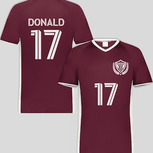 May include: Maroon soccer jersey with white trim and the number 17. The back of the jersey displays the name "DONALD" above the number 17. The front features a "SOCCER CLUB" emblem and the number 17.