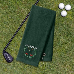A green towel with a golf club and three golf balls on a grassy surface.