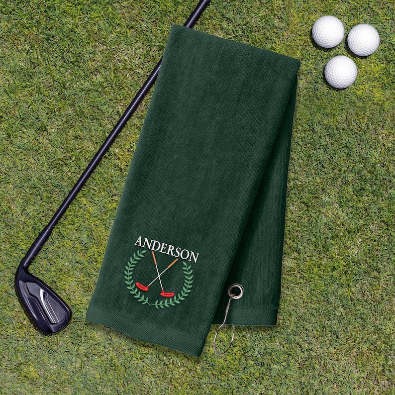 A green towel with a golf club and three golf balls on a grassy surface.
