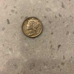 May include: A silver-colored coin with a profile of a woman's face on one side. The coin has the words "Liberty" and "In God We Trust" inscribed on it.