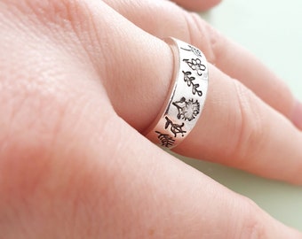 May include: A silver ring with a band of small engraved floral designs. The ring is worn on a person's finger.