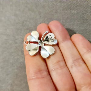 May include: Silver charm shaped like a four-leaf clover with the words "Good Luck" inscribed on one of the leaves.