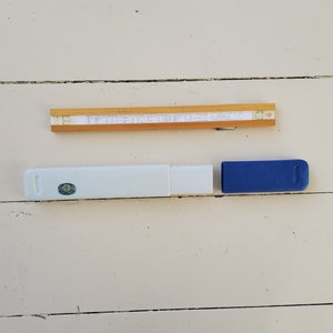 Pode incluir: Uma régua de cálculo de madeira com uma caixa azul e branca. A régua de cálculo está em uma caixa de madeira com uma tampa azul.