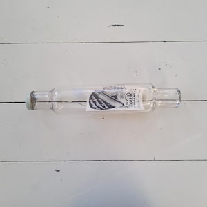 Può includere: Un mattarello di vetro trasparente con un'etichetta che recita "The Roll-Rite Rolling Pin, Winkler, Manitoba". Il mattarello ha un corpo cilindrico con manici in vetro trasparente ad ogni estremità.