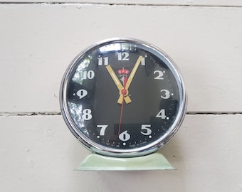 May include: A vintage silver alarm clock with a black face and white numbers. The clock has a green base and says "Made in China" on the face.