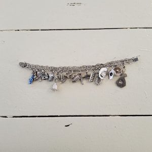 Op de afbeelding: Een zilveren armband met bedels, waaronder een bel, een schoen, een hoed en een hoefijzer.