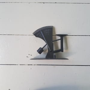 Op de afbeelding: Een vintage zwarte metalen weegschaal met een gebogen wijzerplaat en een klein platform. De weegschaal heeft een contragewicht en een voet. De wijzerplaat leest "GATES, TOLEDO, OHIO, U.S.A.". De weegschaal wordt waarschijnlijk gebruikt om gewicht te meten.