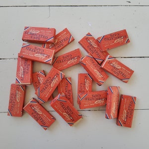 Op de afbeelding: Een verzameling vintage oranje en witte kartonnen dozen met de tekst "Kilgore Disc Caps Extra Loud Safe and Harmless Lubricated Caps" erop gedrukt.