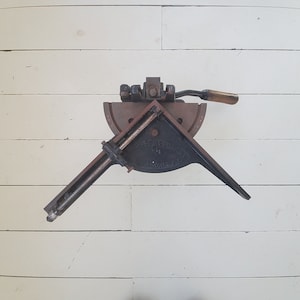May include: A black metal corner clamp with a wooden handle. The clamp has a protractor and a scale for measuring angles. The clamp is used for woodworking.