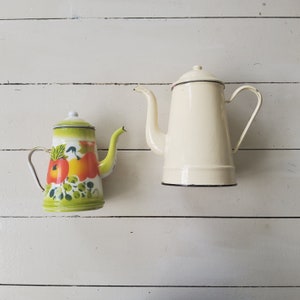 May include: Two vintage enamel coffee pots. One is white with a black rim and the other is green with a fruit pattern.