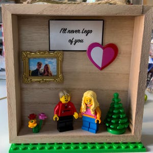 May include: A wooden shadow box with a Lego couple, a small picture frame with a photo of a couple, a heart, and a sign that says "I'll never Lego of you".