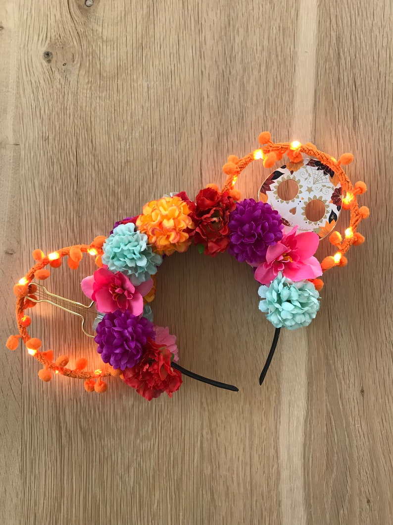 K&ouml;nnte beinhalten: Orangefarbenes und schwarzes Leuchtband mit einem Totenkopf-Motiv und bunten Blumen.