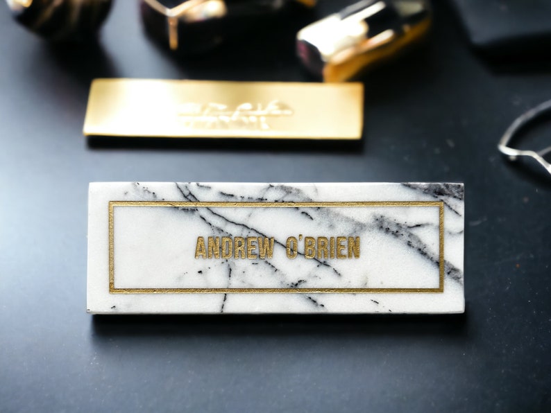 May include: A white marble name card with a gold border and the name "ANDREW O'BRIEN" written in gold lettering.