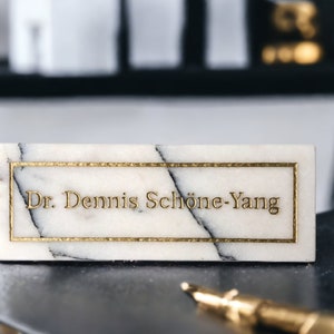 May include: White marble nameplate with gold trim and the text "Dr. Dennis Sch&ouml;ne-Yang" in gold lettering.