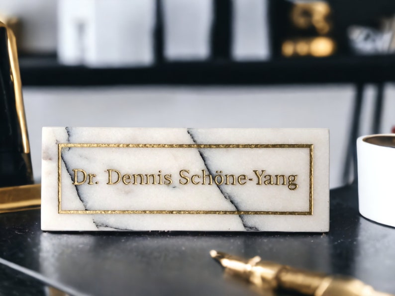 May include: White marble nameplate with gold trim and the text "Dr. Dennis Sch&ouml;ne-Yang" in gold lettering.
