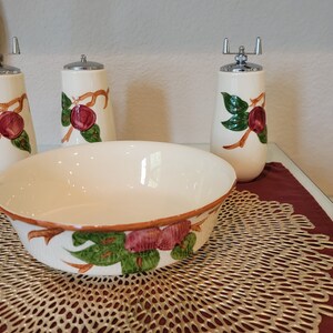 May include: A white ceramic bowl with a green and brown floral design, surrounded by three matching ceramic salt and pepper shakers with a floral design.