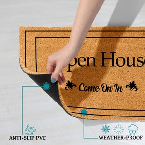 K&ouml;nnte beinhalten: Eine braune Kokosmatte mit schwarzem Text, der "Open House Come On In" mit dekorativen Verzierungen lautet. Die Fu&szlig;matte hat eine schwarze, rutschfeste R&uuml;ckseite und ist wetterfest.