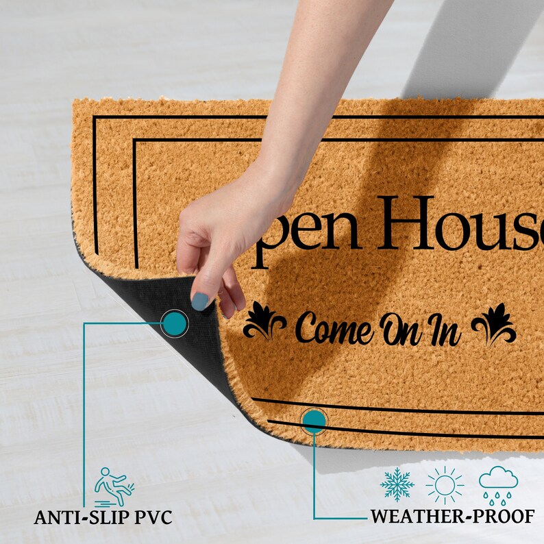 K&ouml;nnte beinhalten: Eine braune Kokosmatte mit schwarzem Text, der "Open House Come On In" mit dekorativen Verzierungen lautet. Die Fu&szlig;matte hat eine schwarze, rutschfeste R&uuml;ckseite und ist wetterfest.