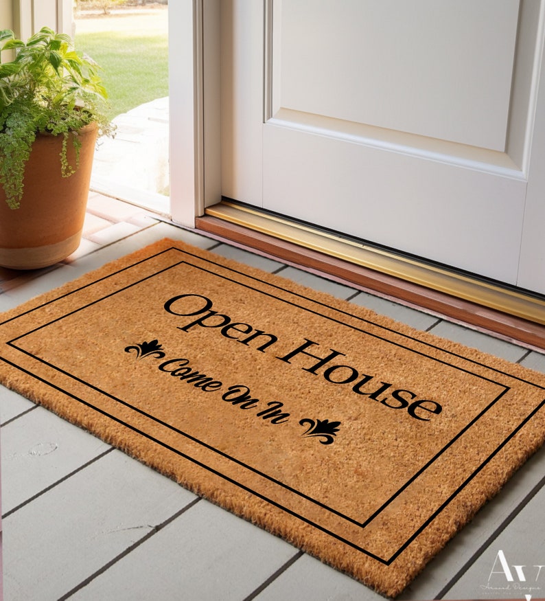 K&ouml;nnte beinhalten: Eine braune Kokosmatte mit schwarzem Rand und dem Text "Open House Come On In" in schwarzen Buchstaben.